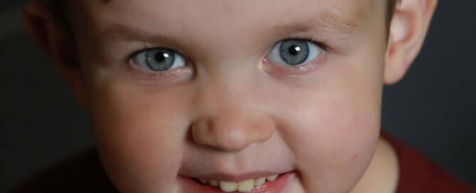 young boy with xxy syndrome wearing a red shirt, smiling at the camera. close up photo.