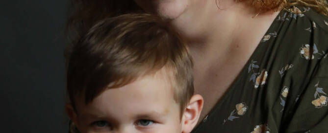 young boy with xxy syndrome wearing red shirt sitting in front of his mom, both smiling.