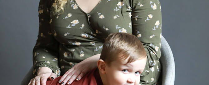 young boy with xxy syndrome wearing red shirt sitting in front of his mom, both smiling.