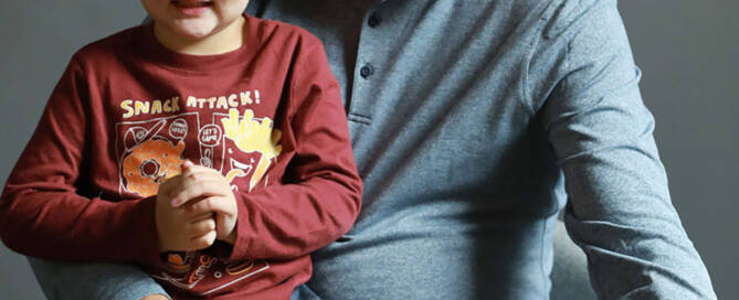 young boy with xxy syndrome wearing red shirt and sitting on his father's lap, both smiling