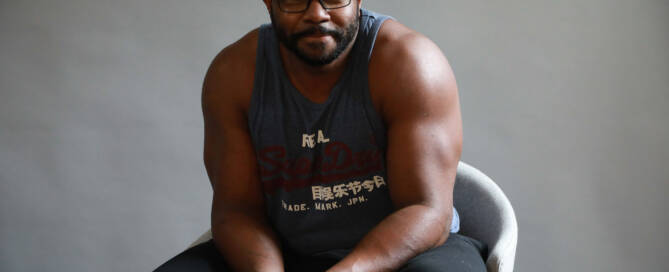 man with xxy wearing glasses and tank top looking into the camera. sitting down