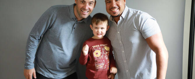 two men and a young boy with xxy syndrome all smile together at the camera