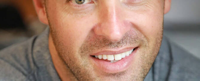 man with xxy syndrome wearing grey buttom up shirt smiling at the camera, close up