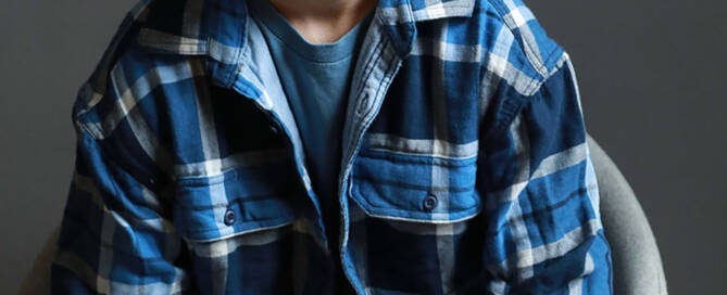 boy with xxy syndrome wearing flannel shirt smiling into the camera.