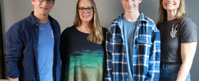 boy with xxy syndrome wearing flannel shirt standing with his family. all smiling into the camera