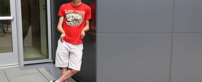 young man with miller syndrome wearing red shirt leaning against wall and looking into the camera